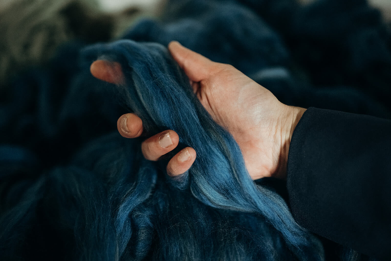 Eine Hand hält sanft blaue Wollfasern, die Textur und Farbe betonen.